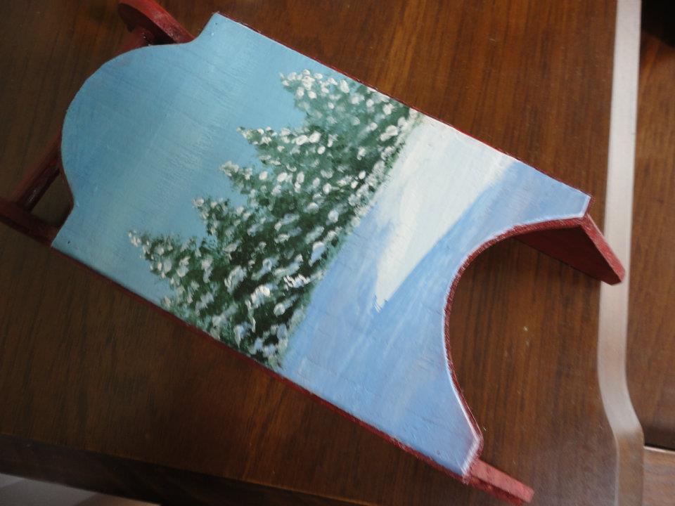 a miniature wooden sled handpainted with snowy trees